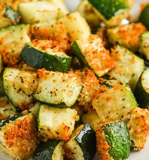 A variety of zucchini dishes including zucchini fritters, zucchini bread, and stuffed zucchini boats on a rustic wooden table.