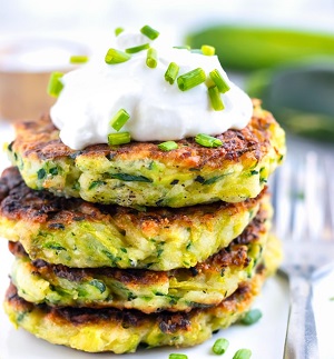 A variety of zucchini dishes including zucchini fritters, zucchini bread, and stuffed zucchini boats on a rustic wooden table.