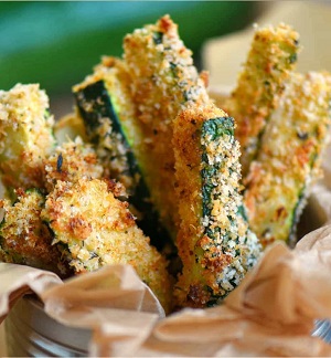 A variety of zucchini dishes including zucchini fritters, zucchini bread, and stuffed zucchini boats on a rustic wooden table.