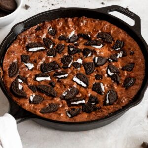 Assortment of camping desserts including campfire apple crisp, campfire cobbler, and campfire brownies prepared in cast iron skillets and foil packets.