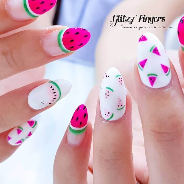 Bright watermelon nails featuring vibrant summer pink and green polish, accented with playful black seeds, perfect for a fresh summer look.