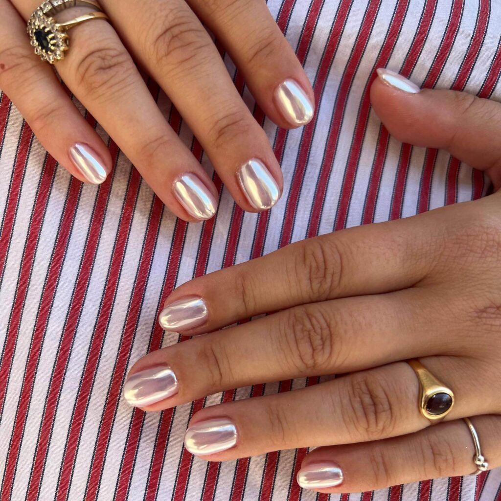 Close-up of hands showcasing various metallic nails designs, including black nails with silver flakes, dark gold nail polish, and metallic red acrylic nails.