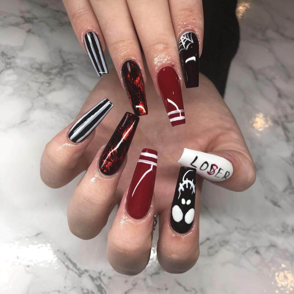 A set of Halloween acrylic nails with spooky nail designs, including black and red accents, ghosts, and candy corn-themed nails.