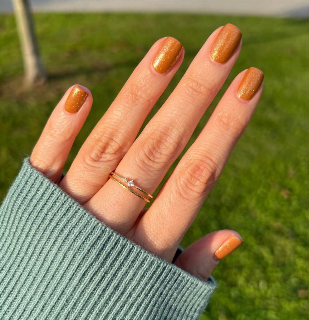 Close-up of warm-toned pumpkin spice nails with a fall-inspired design.